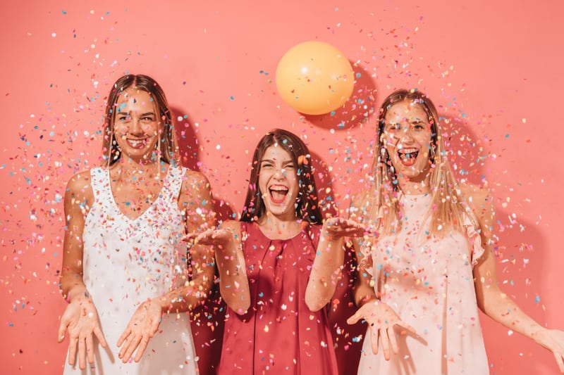 Tres mujeres mirando a la cara, sonriendo, mientras que hay escarcha y globos frente a ellas.