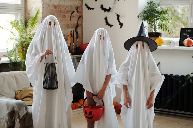 Tres personas disfrazadas de fantasmas y con canastas de calabazas de Halloween.