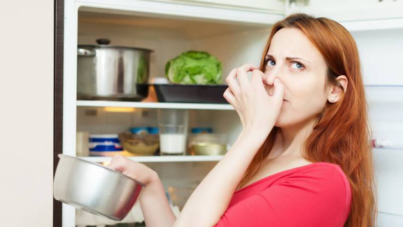 Mujer tapándose la nariz y sacando ollas del refrigerador.