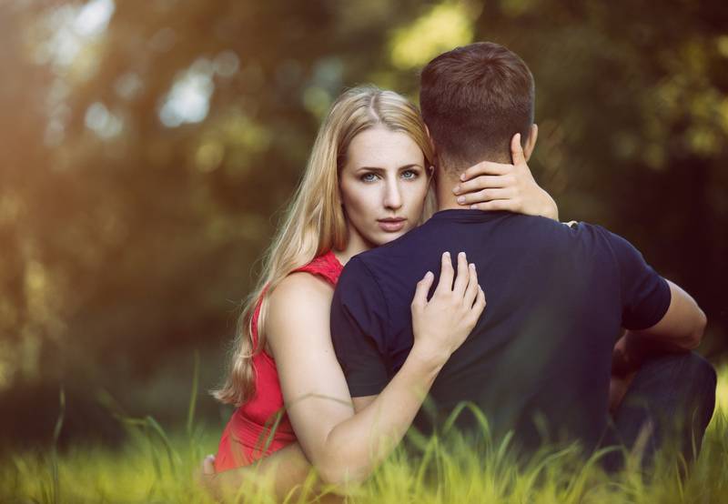 Una pareja sentada sobre el pasto. Él está de espaldas a la cámara, mientras que ella está mirando de frente.