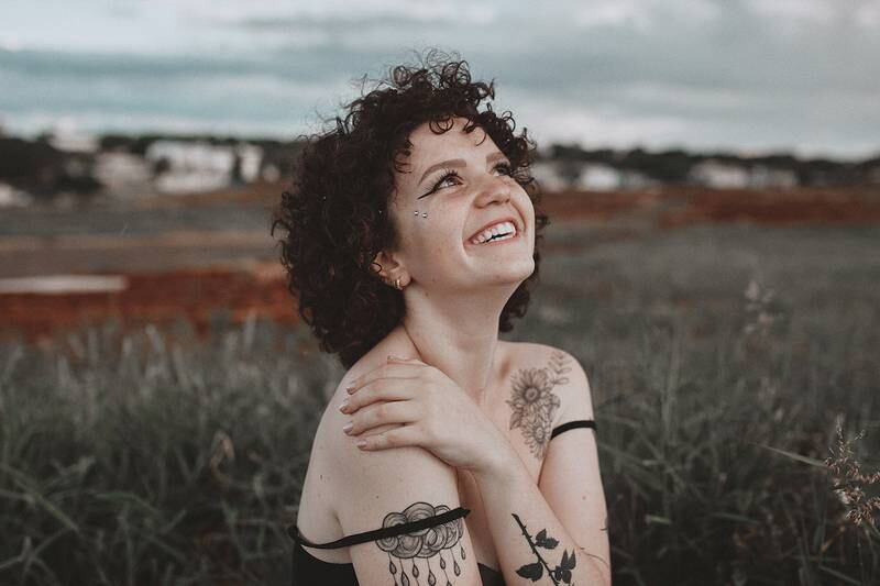 Mujer con tatuajes, mirando feliz hacia el cielo.