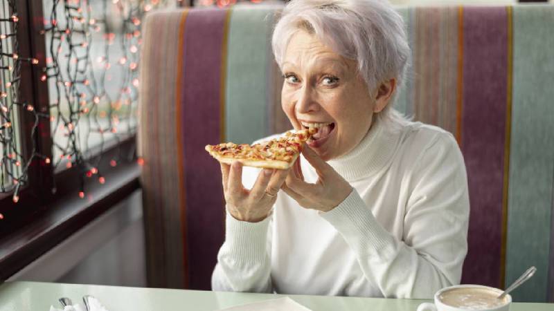 Mujer de la tercera edad comiendo pizza.