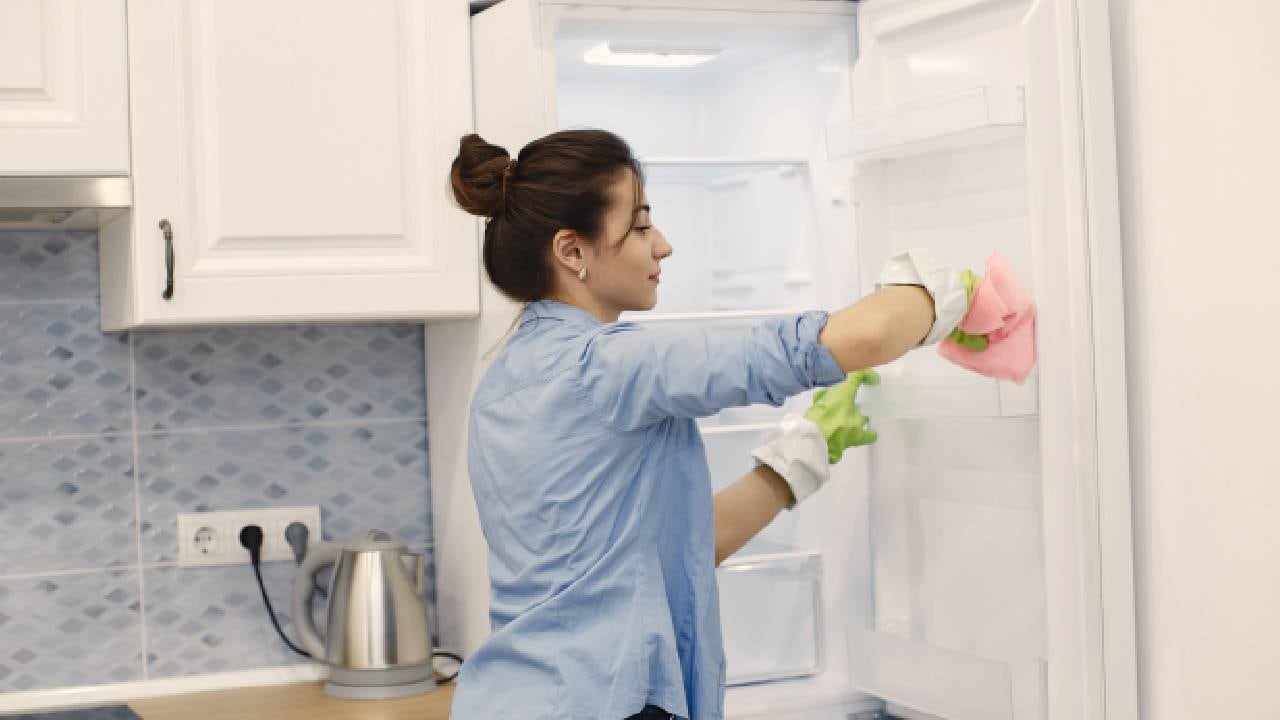 Mujer con camisa azul limpiando el refrigerador.