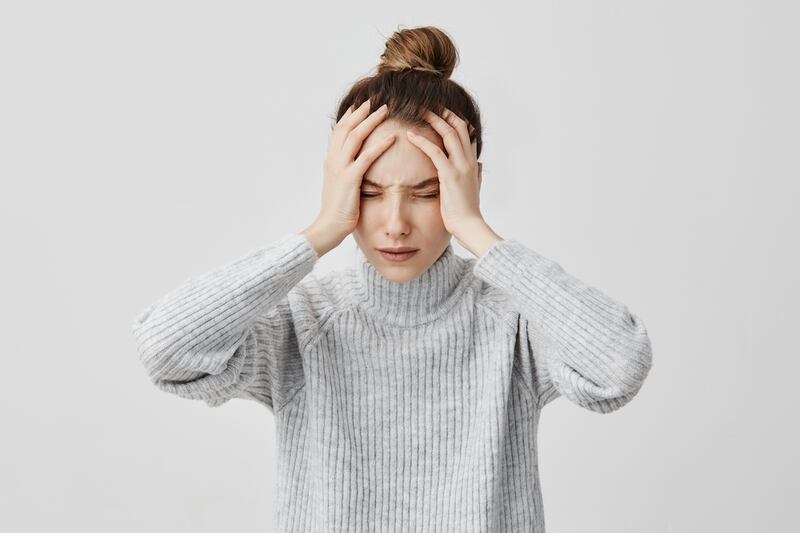 mujer parada, tomándose la cabeza y con cara de dolor.