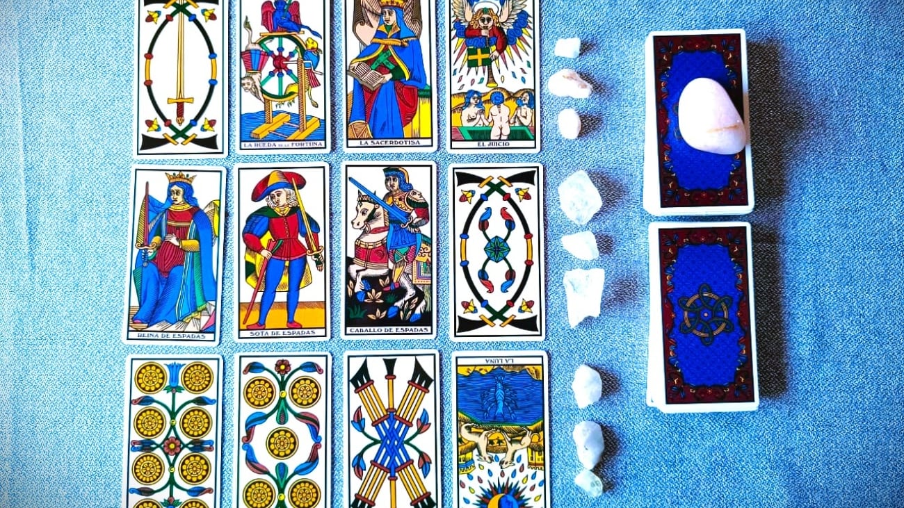 Cartas de Tarot sobre un paño gris. A la derecha está el mazo cortado en dos. Entre el mazo y la tirada hay una hilera de cuarzos blancos.