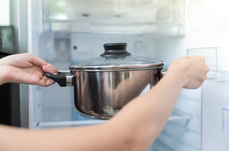 Persona guardando una olla con tapa a un refrigerador.