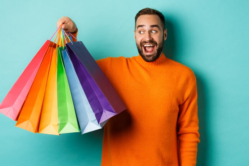 Hombre sosteniendo seis bolsas con compras y mirándolas feliz.