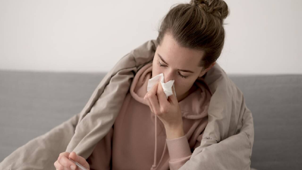 Mujer con cobija café encima limpiando su nariz.